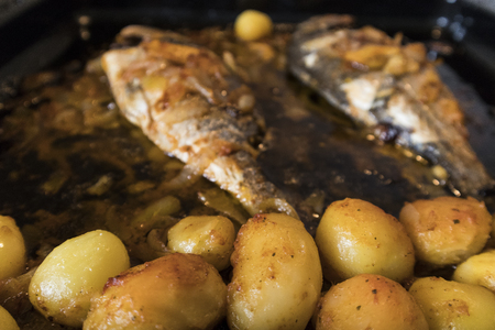 Fish baked in the oven, golden with boiled potatoes and olives in white dish. Typical Portuguese dish.の写真素材