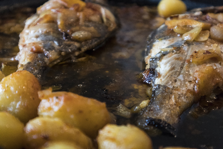 Fish baked in the oven, golden with boiled potatoes and olives in white dish. Typical Portuguese dish.の写真素材