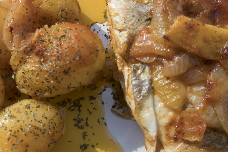 Fish baked in the oven, golden with boiled potatoes and olives in white dish. Typical Portuguese dish.の写真素材