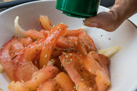 Tomato salad seasoned with onions and oregano. Woman's hand to temperの写真素材