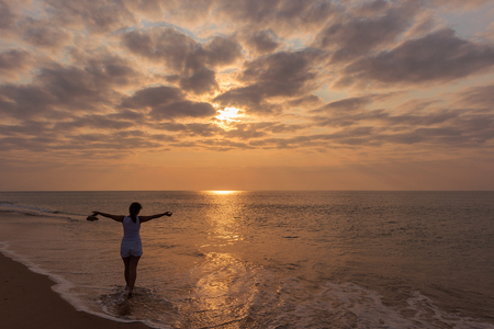 Silhouette of young girl with open arms, with sunset and dramatic sky.の写真素材