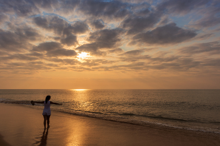 Silhouette of young girl with open arms, with sunset and dramatic sky.の写真素材