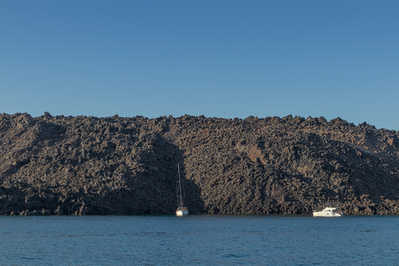 sailboat with cliff behind in the sea of santorini.の写真素材
