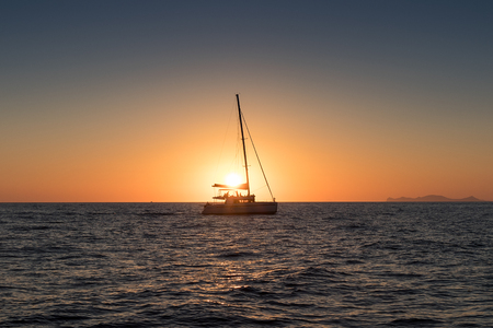 Beautiful sunset in Oia, Santorini, seen from the sea with silhouette of catamaran.の写真素材