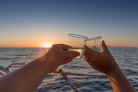 couple toasting with two glasses of white wine overlooking the sea and sunset.の写真素材