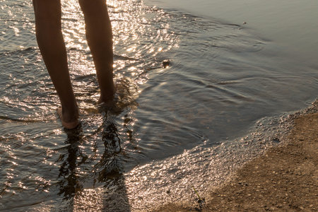 African young girl's legs to walk over the water with sunset light.