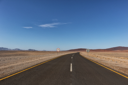 Asphalt road crossing the Namibia Desert on the way to Sossusvlei. With speed limit sign.の写真素材