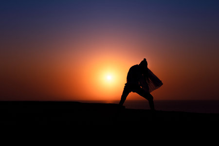 Silhouette of African girl on hill top posing and dancing with sunset view and ocean view.の写真素材