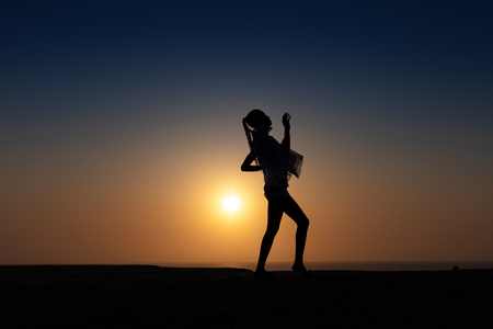 Silhouette of African girl on hill top posing and dancing with sunset view and ocean view.の写真素材