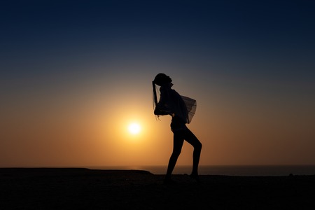 Silhouette of African girl on hill top posing and dancing with sunset view and ocean view.の写真素材