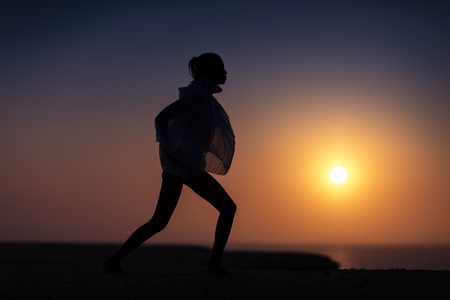 Silhouette of African girl on hill top posing and dancing with sunset view and ocean view.の写真素材