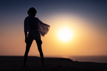 Silhouette of African girl on hill top posing and dancing with sunset view and ocean view.の写真素材