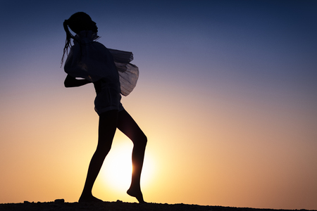 Silhouette of African girl on hill top posing and dancing with sunset view and ocean view.の写真素材
