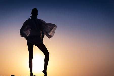 Silhouette of African girl on hill top posing and dancing with sunset view and ocean view.の写真素材