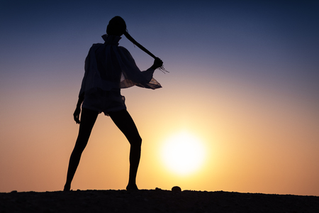 Silhouette of African girl on hill top posing and dancing with sunset view and ocean view.の写真素材
