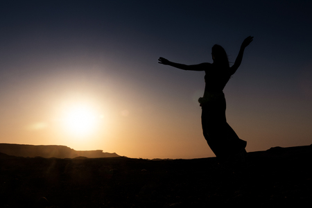 Woman dancing to the famous Arab belly dance. With sunset in the arid desert plain of Namibe. Africa. Angola.の写真素材