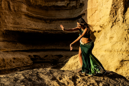 Young girl in green dress dancing the famous belly dance, in the mythical space of the canyons of the Namibe desert. Africa. Angola.の写真素材