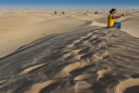 UAE/ABUDHABI - 13 DEZ 2018 - Photograph of woman sitting on top of a Dune in the desert of Abu Dhabi. UAEのeditorial素材