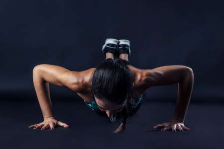 woman performing fitness exercises isolated on dark background.の写真素材
