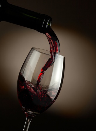 Red wine pouring in glass over dark backgroundの写真素材