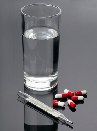 Pills, thermometer and glass of water over black backgroundの写真素材