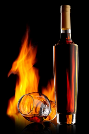 Bottle and glass of cognac over dark background with flameの写真素材