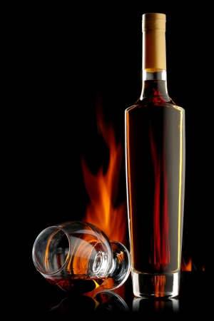 Bottle and glass of cognac over dark background with flameの写真素材