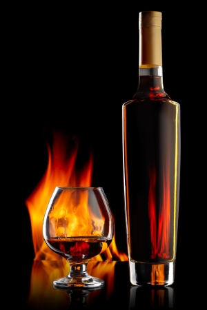 Bottle and glass with cognac over dark background with flameの写真素材