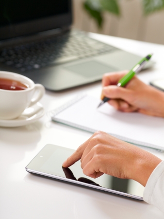 Woman hands with tablet PC and notepad at officeの写真素材