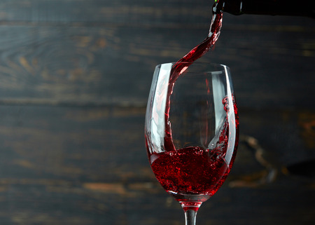Pouring red wine into the glass against dark wooden backgroundの写真素材