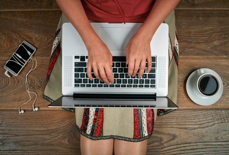 Woman with laptop, smartphone and coffee sitting on wooden floorの写真素材