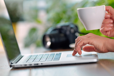 Woman viewing photos from camera on her laptop. Hand with cup of coffee. Shallow DOFの写真素材