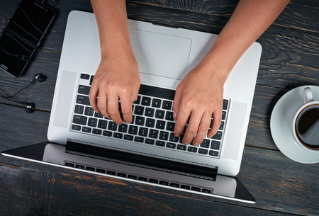 Woman's hands with laptop, smartphone and coffee. Dark vintage wooden background. Top viewの写真素材