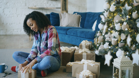 Attractive mixed race girl packing gift box near Christmas tree at homeの写真素材
