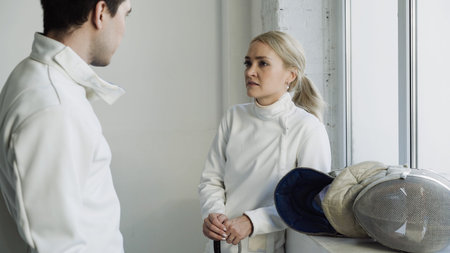 Two young smiling fencers man and woman sharing experience during break of fencing match indoors