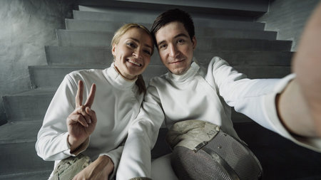 POV of Two young smiling fencers man and woman taking selfie on smartphone camera after fencing...