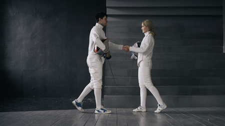 Two fencers man and woman shake hands each other at the end of fencing competition indoorsの写真素材