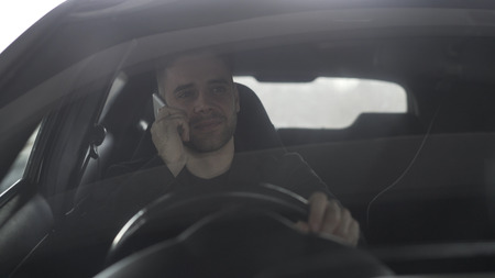 Attractive happy businessman chatting smart phone while sitting inside his car outdoorsの写真素材