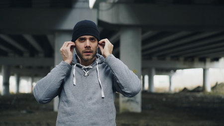 Handsome sportive man runner putting on earphones and starts running at urban outdoors city location...