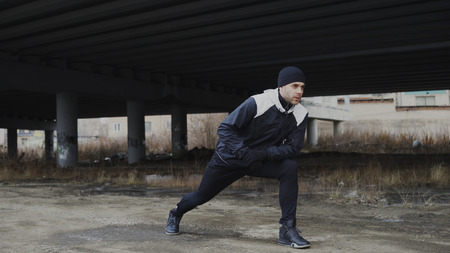 Attractive man runner doing stretching exercise for morning workout and jogging at urban location outdoors in winterの写真素材