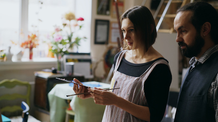 Skilled artist man teaching young woman painting on easel at art school studio - creativity, education and art people conceptの写真素材