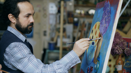 Concentrated man artist painting still life picture on canvas in art studio indoorsの写真素材