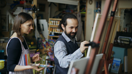 Skilled artist teacher showing and discussing basics of painting to student at art-classの写真素材