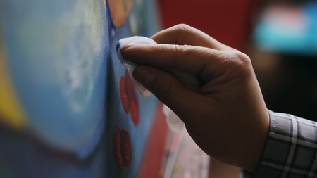 Close-up of artists hand smearing oil paints on canvas picture in art workshopの写真素材