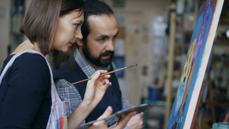Skilled artist teacher showing and discussing basics of painting to student at art-class