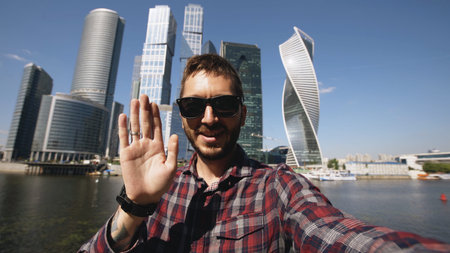 Happy tourist man having online video chat using his smartphone camera near international business...