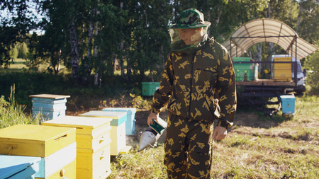 Young beekeeper man smoking bees away from beehive in apiaryの写真素材