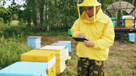 Beekeeper man with tablet computer checking wooden beehives before harvesting honey in apiaryの写真素材