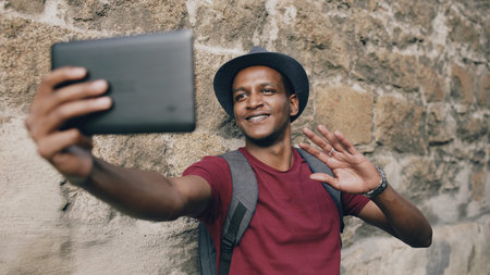 Happy african american tourist man having online video chat using tablet computer while travelling...