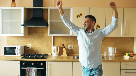 Handsome young funny man dancing in kitchen at home in the morning and have fun on holidaysの写真素材